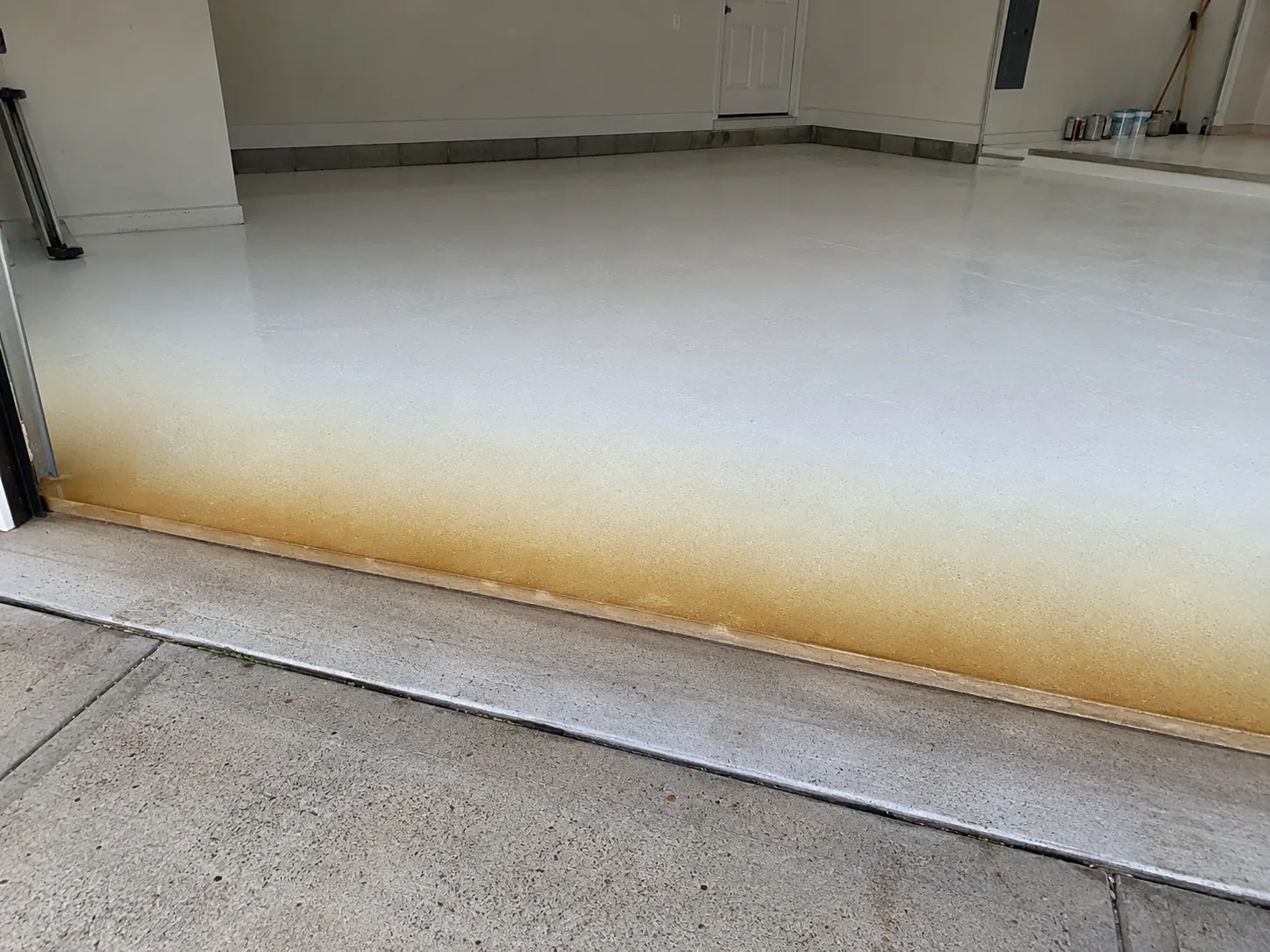 White epoxy floor coating ambered to yellow-brown in a band near the garage door