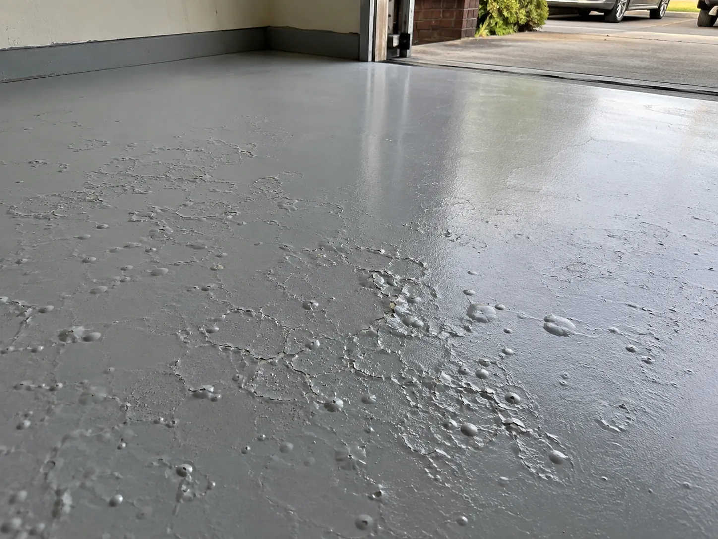 Grey epoxy garage floor covered in small round moisture blisters, some burst open