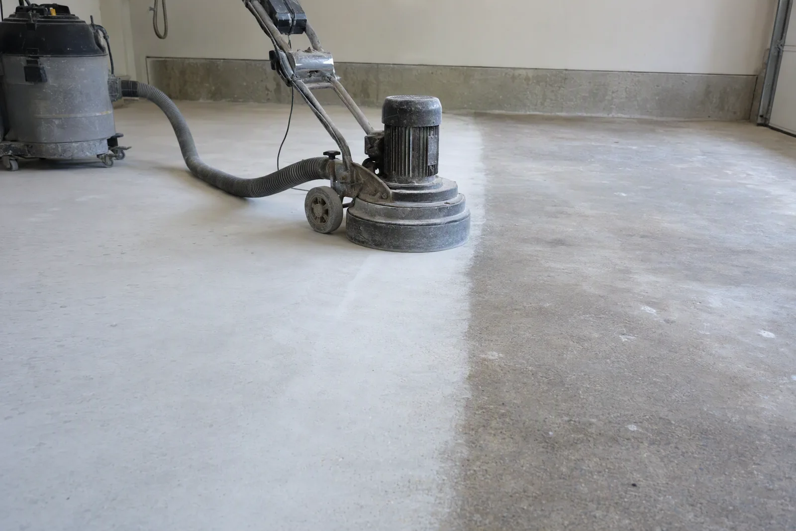 Walk-behind concrete grinder mid-pass showing freshly ground lighter concrete beside old stained slab
