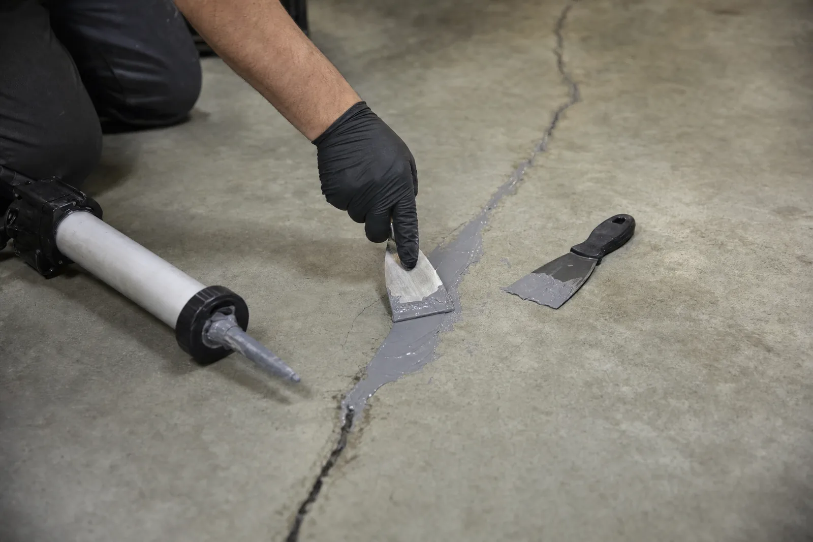 Gloved hand troweling polyurea crack filler into a routed crack in a bare concrete floor