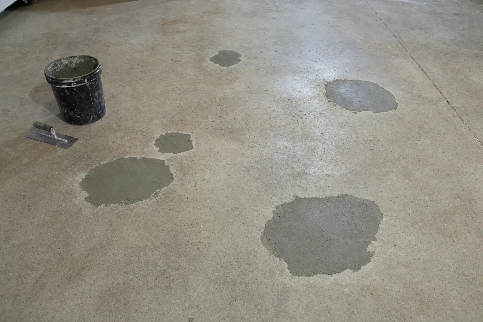 Bare concrete garage floor with several spalled areas patched with fresh grey repair mortar
