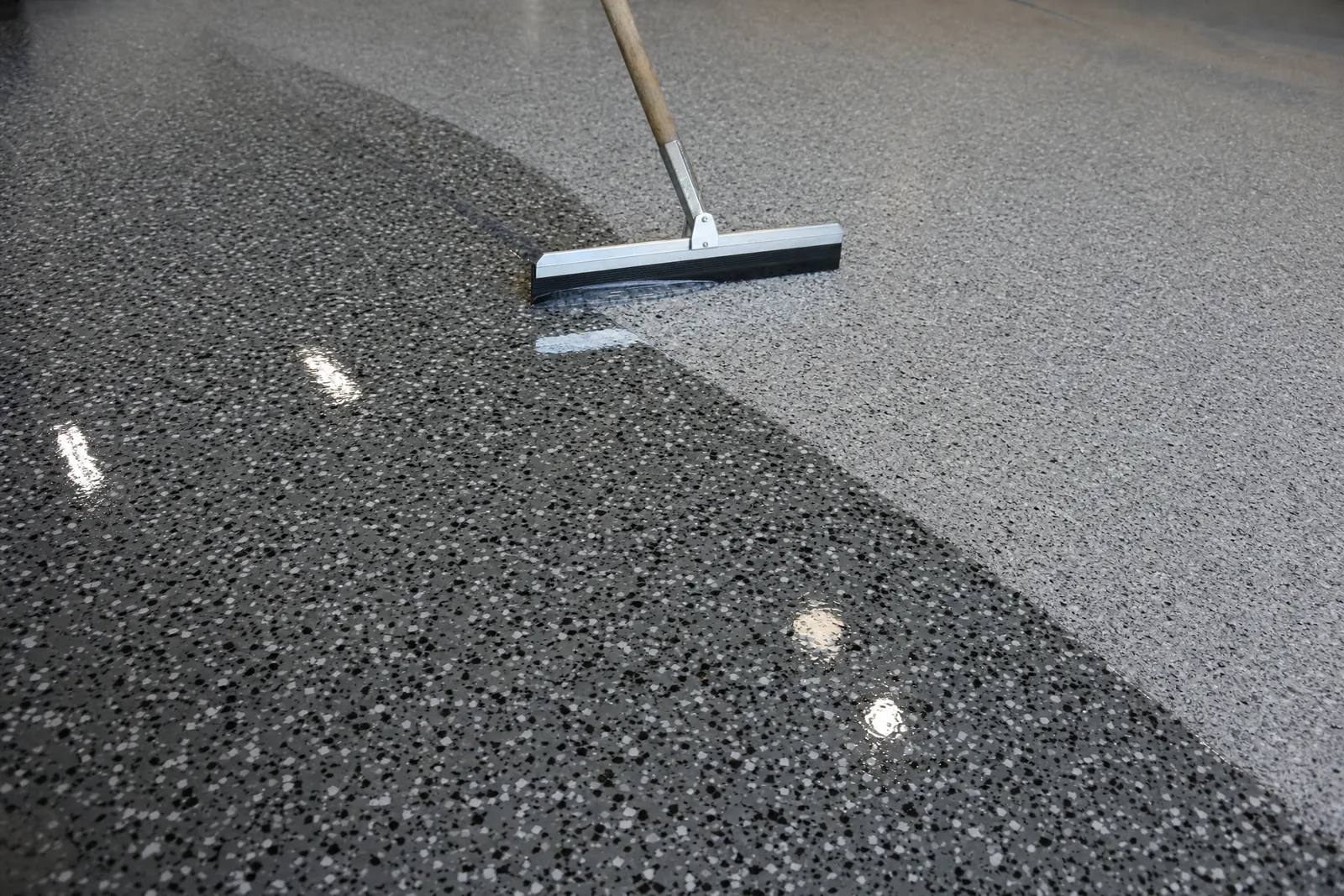 Clear polyaspartic topcoat being squeegeed across a finished flake floor
